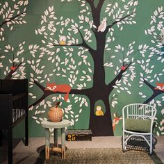 a room with a tree painted on the wall next to a white chair and table