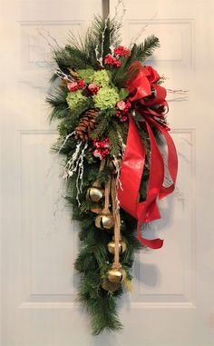 a christmas wreath hanging on the front door with bells and greenery in red ribbon