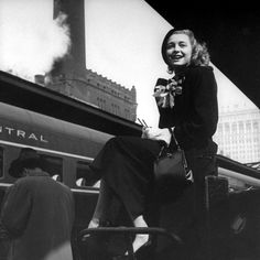 a black and white photo of a woman sitting on a chair in front of a train