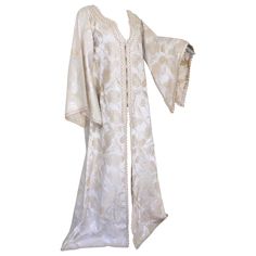 Elegant Moroccan white ivory and old brocade kaftan embroidered with gold trim threads. Size L to XL circa 1980s. This long maxi dress kaftan is embroidered and embellished entirely by hand. One of a kind evening Moroccan Middle Eastern gown. The kaftan features a traditional neckline and embellished sleeves. In Morocco, fashion preserves its traditional style inherited from great civilizations that found their way to Northwest Africa, such as the Ottomans and the Moors. Moroccan fashion has bee White Silk Kaftan For Festive Occasions, Silk Tunic Kaftan For Wedding, Long Embroidered Formal Kaftan, Formal Long Embroidered Kaftan, Traditional Maxi Length Wedding Kimono, Elegant Long Kaftan With Intricate Embroidery, Elegant Long Thobe With Intricate Embroidery, Gold Embroidered Floor-length Thobe, Embroidered Gold Floor-length Thobe