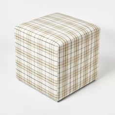 a white and brown checkered ottoman sitting on top of a white floor next to a wall