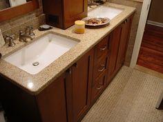 two sinks in a bathroom with brown cabinets and marble counter tops, one has a plate of food on it