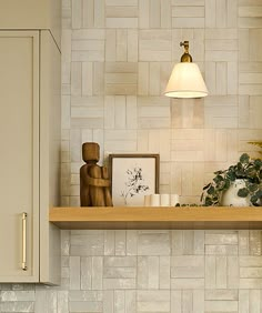 a kitchen with white tiles and wooden shelves on the wall, along with a lamp