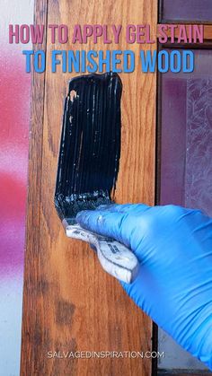 a person in blue gloves is painting the side of a wooden door with black paint