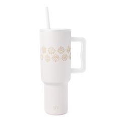 a white coffee cup with gold designs on the side and a straw sticking out of it