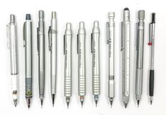 several pens and pencils lined up on a white surface with one pen in the middle