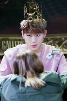 a young man with a crown on his head looking at another person's hair