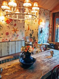 an old wooden table and chairs in a room with floral wallpaper on the walls