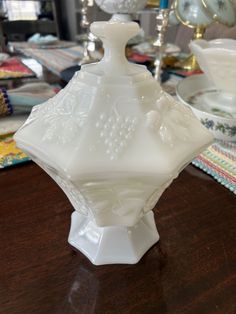 a white vase sitting on top of a wooden table next to other glass dishes and candles