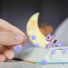 someone is holding a tiny purple teddy bear on a book with stars flying around it