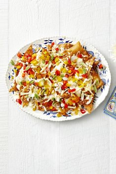 a white plate topped with nachos covered in cheese and toppings next to a flower