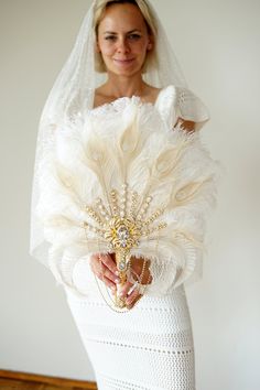 a woman in a wedding dress holding a white feathered veil and brooch on her head