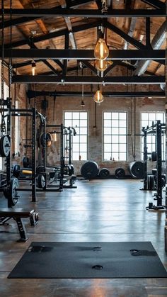 an empty gym with lots of machines and lights hanging from the ceiling in front of large windows