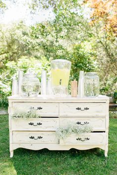 an old dresser with vases and glasses on it in the middle of some grass