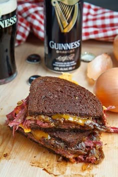 a sandwich cut in half sitting on top of a cutting board next to onion and beer