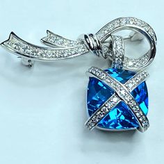 One 18k White Gold Dangle Lady Diamond Brooch. Featuring One Faceted Checkerboard Size London Blue Topaz Dangling Down From A Bow Ribbon Diamond Frame. The Topaz Embellished With Diagonal "X" On Top, It Pave Setting Eighty-Five (85) Round Brilliant Diamonds On The "X" And The Ribbon Frame, Combine Approx. 1.00ct, Being E-F Color And Vs1 Clarity. The Topaz Is 14.0 X 14.0mm, A Quality, The Dangle Is 15.08 X 15.08mm, The Ribbon Bow Is 1.5" X 3/8", Hanging Length Is 2 1/4", Weight 13.6gm, Hallmark 1 Anniversary Jewelry: Brilliant Cut Blue Topaz, Luxury Pear-shaped Blue Topaz Jewelry, Blue Topaz Pendant With Diamond Accents, Brilliant-cut Blue Topaz Jewelry, Luxury Multi-stone Blue Topaz Gemstones, Diamond Frame, Pave Setting, Diamond Brooch, London Blue