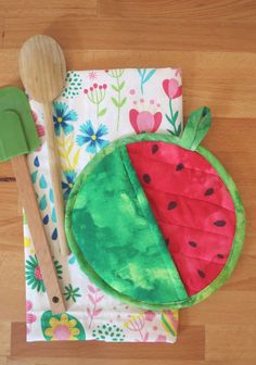 a wooden spoon and fork sitting on top of a table next to a cloth with a slice of watermelon