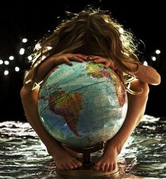 a woman holding a globe in her hands while sitting on the ground with water around her