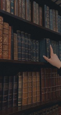 a hand reaching for an old book on a bookshelf filled with many books