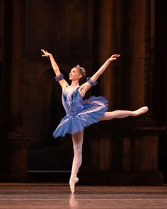 the ballerina is wearing a blue tutu and has her arms outstretched in the air