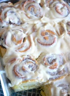 a pan filled with cinnamon rolls on top of a blue table cloth covered in icing