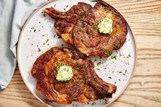 two steaks on a white plate with green garnish