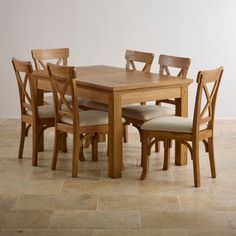 a wooden table with six chairs around it on a tile flooring area in front of a white wall