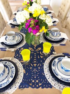 a table set with blue and white plates, flowers in a vase on the center