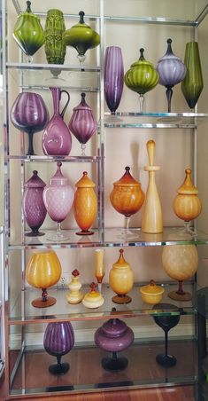 many different colored vases are on display in a glass case with metal shelves holding them