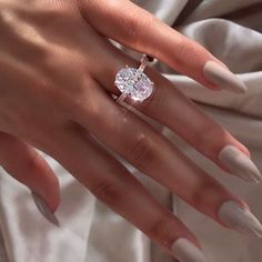 a woman's hand with white manicured nails and an oval shaped diamond ring