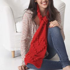 a woman sitting on the floor wearing a red knitted scarf with pom - poms