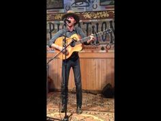 a man singing into a microphone while holding an acoustic guitar in front of him and wearing a cowboy hat