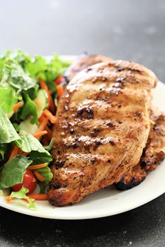 a white plate topped with meat next to a salad and lettuce covered in sauce