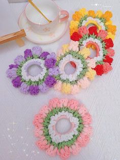 four crocheted flowers sitting on top of a table next to a cup and saucer