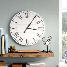 a white clock mounted to the side of a wall next to a book shelf with books on it