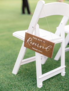 a white chair with a wooden sign hanging from it's back on the grass