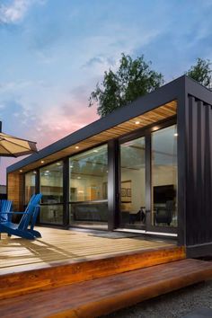 a house made out of shipping containers with blue chairs and an umbrella on the deck