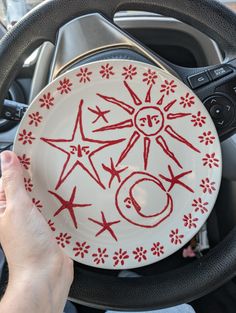 a person holding a plate with red designs on it in the drivers seat of a car