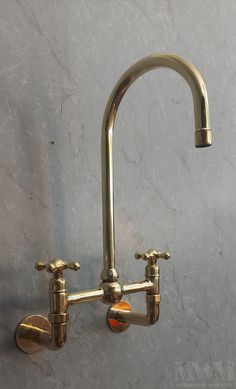 two brass faucets on the wall in a bathroom with marble walls and flooring