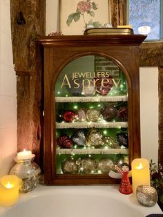 a lighted display case in the corner of a bathtub filled with ornaments and candles