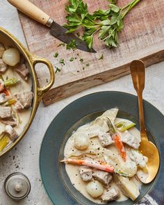 a bowl of soup with meat and vegetables in it next to a wooden cutting board