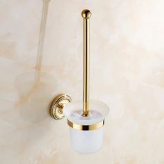 a gold toilet brush and holder on a marble wall