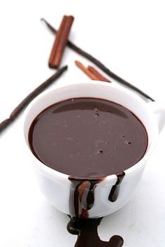 a chocolate sauce in a white bowl with cinnamon sticks sticking out of the side and on top