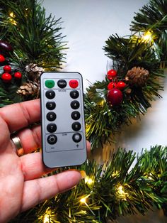 a hand holding a remote control in front of a christmas wreath with lights on it