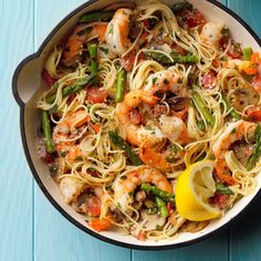 a skillet filled with shrimp, pasta and asparagus on top of a blue table