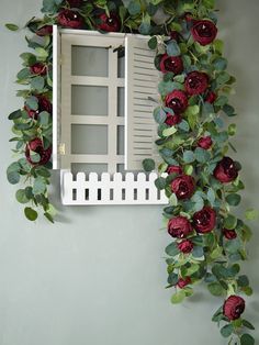 a white window with red flowers and green leaves on the outside, hanging from a wall