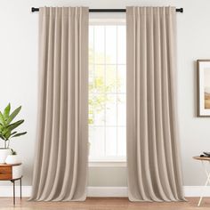 a living room with white walls and beige drapes on the windowsill, along with a potted plant