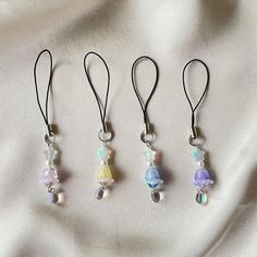 four necklaces with different colored beads hanging from them on a white fabric background,