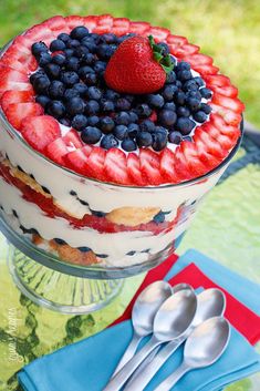 a cake with berries and blueberries on top is sitting on a glass plate next to two spoons