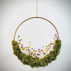 a wreath with flowers and moss hanging from the ceiling in front of a white wall